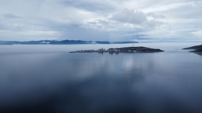 Still water and overcast sky with a small island and a mountain range in the background.