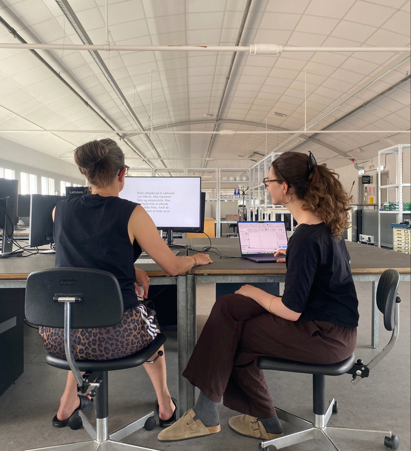 Photograph of mock experimental set-up at the Academy showing Gwenllian sat next to a participant while they read a passage of text on a computer monitor.