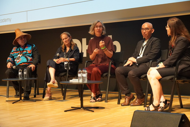 Fem paneldeltagere sidder på en scene under en debat, mens den midterste taler og gestikulerer.