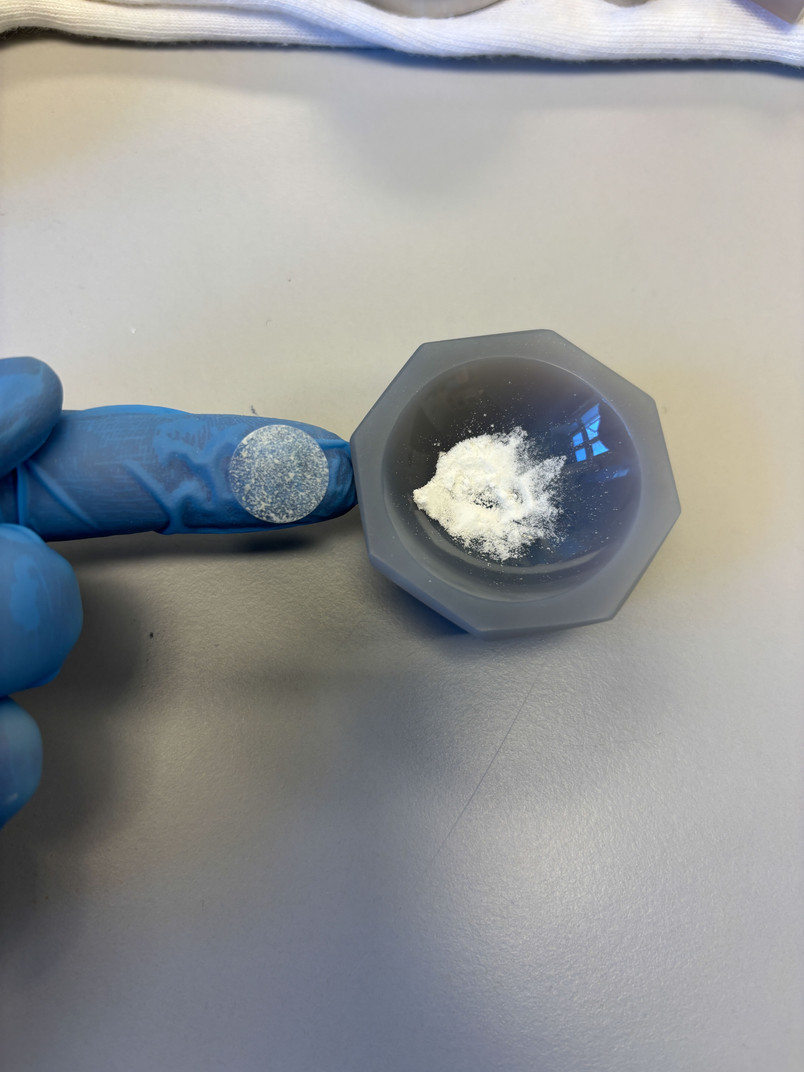 Knust pulver i en morter og en finger indeni en blå handske.