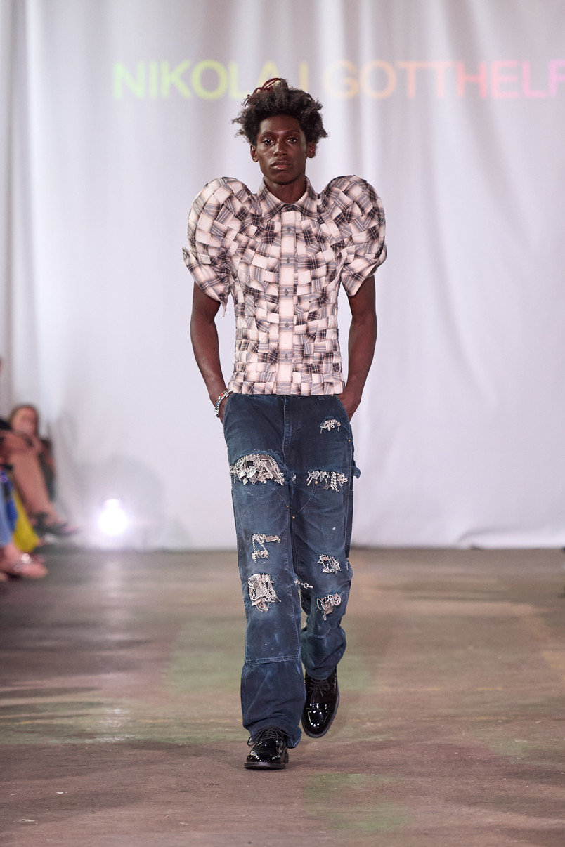 Model på catwalk iført ternet top med markante puffærmer og slidte mørkeblå jeans.