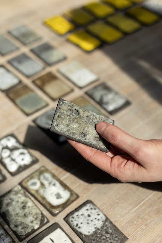 a hand holding a glaze test, more laying on the table in the background