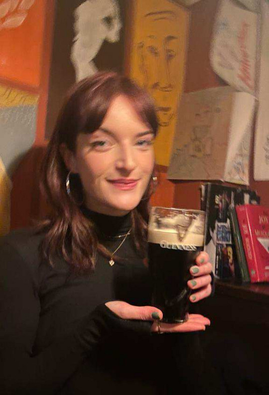 A young woman holding a cracking pint of Guinness with the G perfectly split.