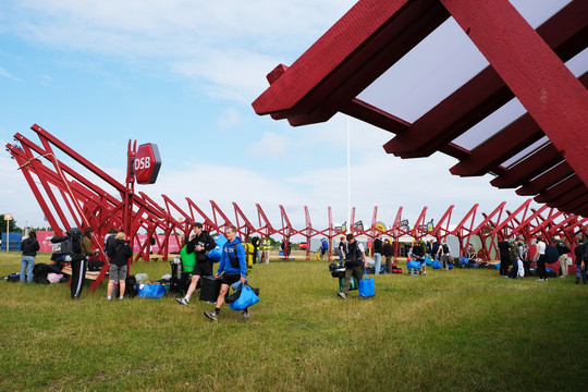 Røde bærebjælker i cirkelkonstruktion. Festivalgæster ankommer.