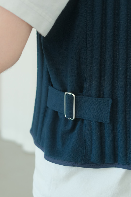 Detalje af mørk vest med justerbar strop og metalspænde i siden.