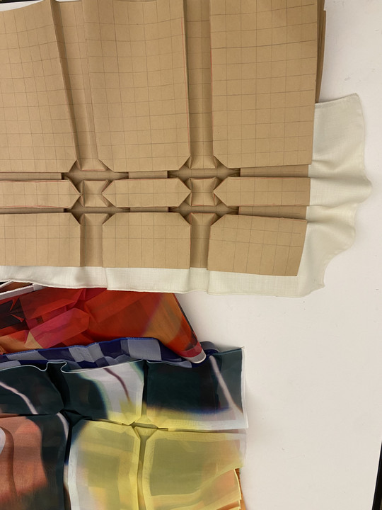  To stykker stof, ét med farverigt mønster og ét med beige, geometrisk foldet design.