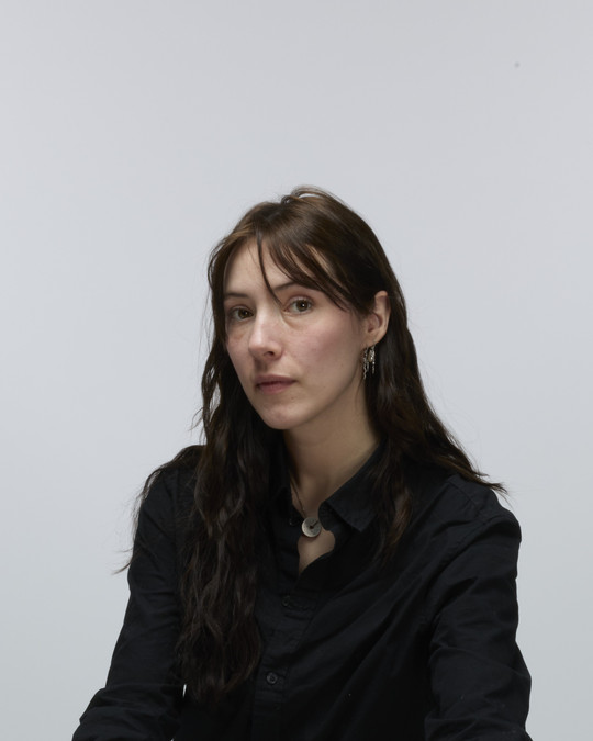 An image of the designer, a young woman with long, dark hair wearing a black shirt and a silver necklace