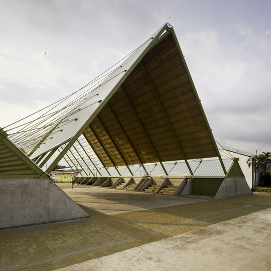 Åben pavillon med højt skråt tag over en udendørs bane.
