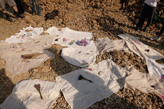 White textiles with plants, stones and other objects spread across rocky ground.