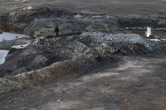 Person walking through a dark excavated landscape with piles of rock and soil.