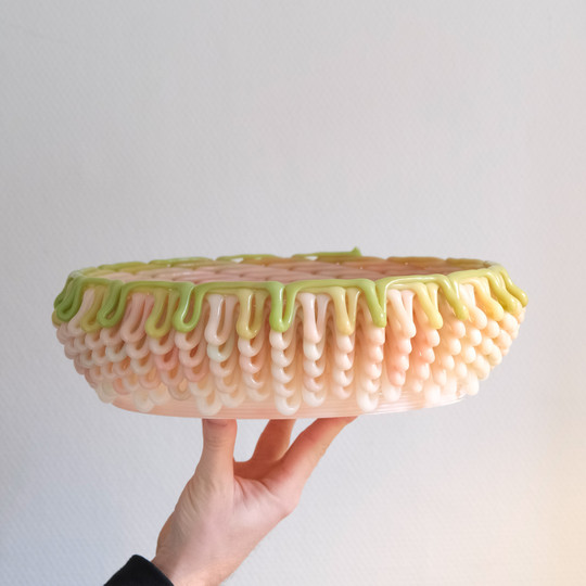 Hand holding a bowl-shaped object layered with glossy loops in pastel colors.