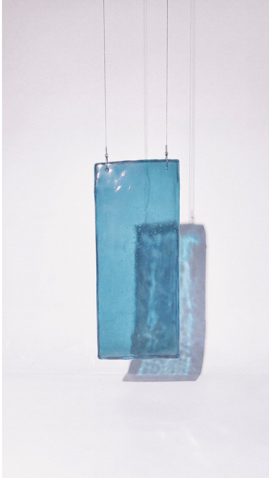 Transparent blue glass panel suspended by thin wires, casting a blue shadow.