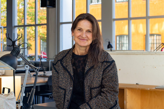 Smilende kvinde i et lyst arbejdsrum med store vinduer.