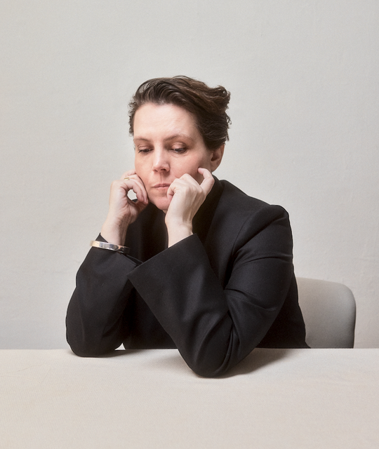 Woman in black sits at a table with her chin resting in her hands.