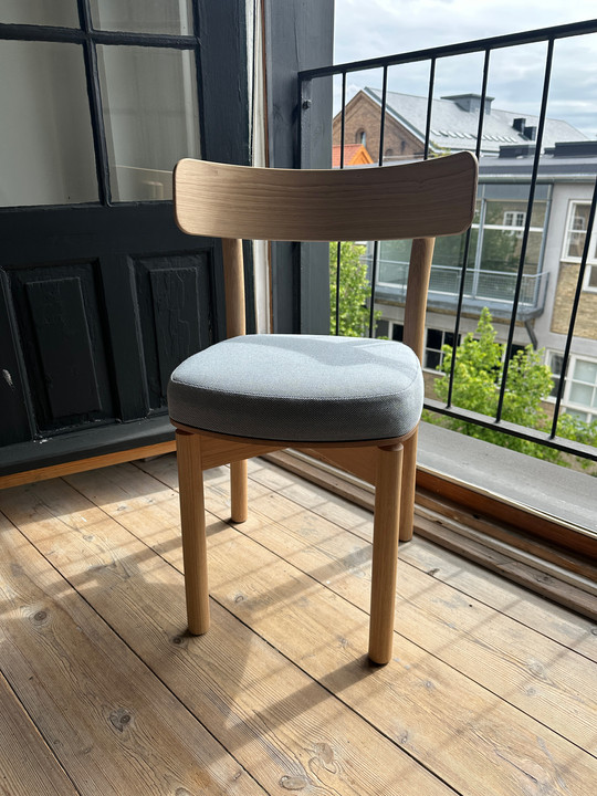 Wooden chair with a light blue seat standing in sunlight by an open balcony door.