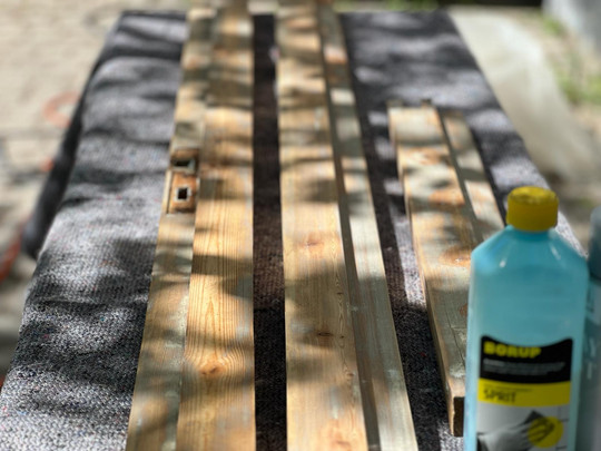 Wooden strips laid on a blanket beside a bottle of wood treatment.