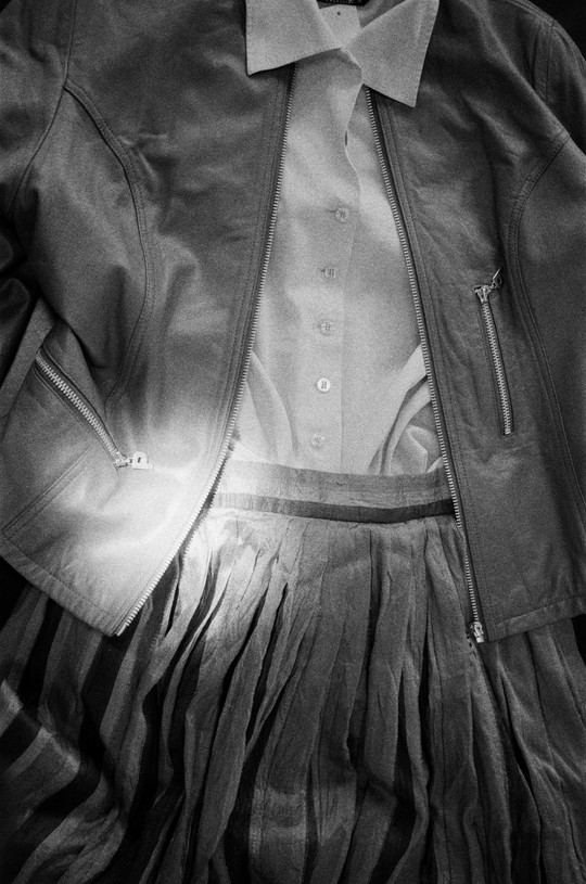 Close-up of a zippered jacket layered over a light shirt and pleated skirt.