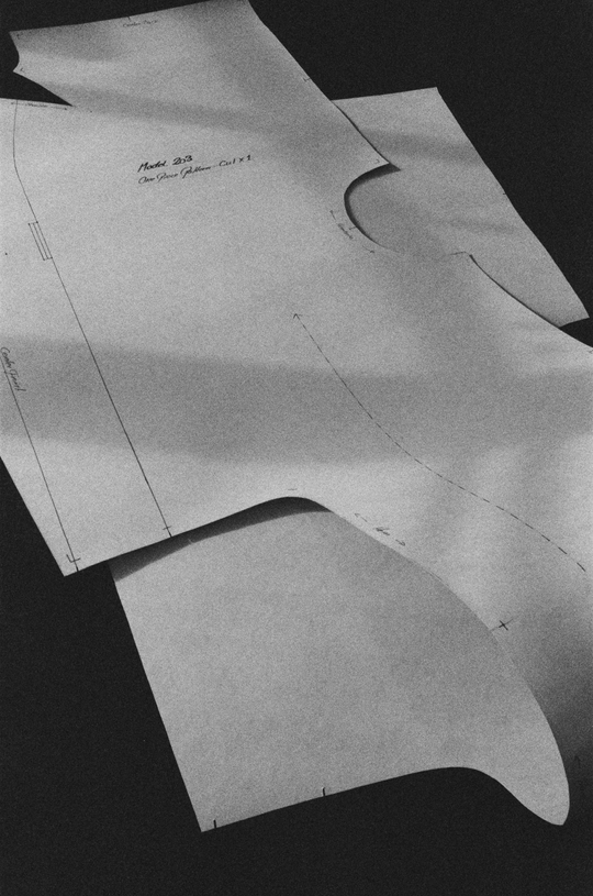 Overlapping paper sewing patterns with drawn lines, arrows and markings on a dark surface.