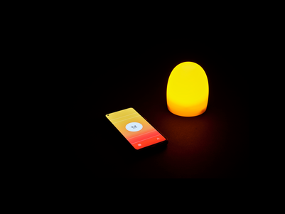 The image shows a smartphone with a orange screen displaying blood sugar levels at 6,14mmol, placed next to a small, glowing orange lamp, both in a dark environment
