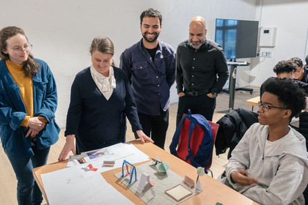 Fire mennesker står rundt om bord, hvorpå der er en model af en legeplads. Ung dreng sidder ved siden af bordet.
