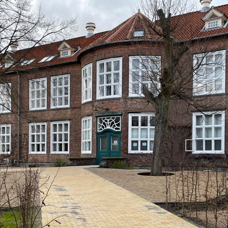 Murstensbygning med store hvide vinduer og brolagt sti foran.