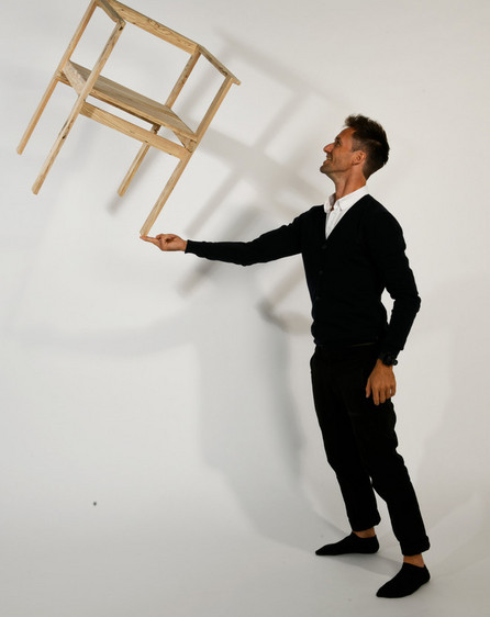 Person balancerer en træstol på en finger i et fotostudie.
