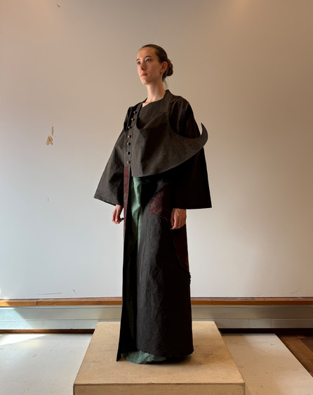 Model wearing a dark layered garment inspired by a moving temple, with an extended eave-like structure and faded textile surfaces suggesting incense smoke, time, wind, and rain.