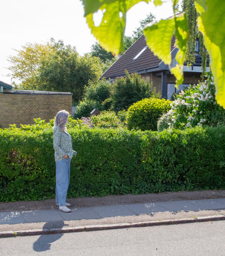 Woman researcher standing in front of a green hedge and a yellow brick house