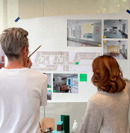 Fire personer studerer plantegninger og visualiseringer af indretning på en væg.