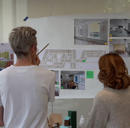 Fire personer studerer plantegninger og visualiseringer af indretning på en væg.