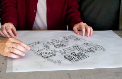 Two people examine a hand-drawn sketch of rooms and furnishings.