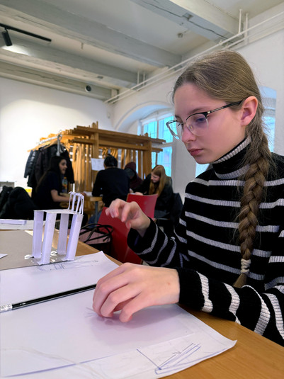 Ung pige med fletning arbejder på en papirmodel af en stol