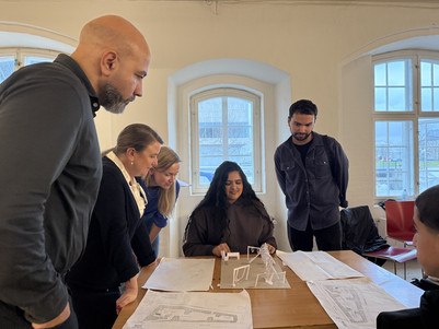 Fire voksne står og ser på en ung pige, der taler om en arkitekturmodel af en legeplads