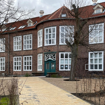 Murstensbygning med store hvide vinduer og brolagt sti foran.