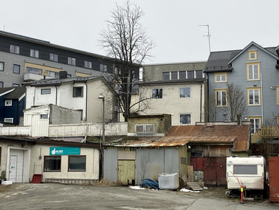 Bebyggelse med ældre, slidte skure foran nyere boligbyggeri på en grå vinterdag
