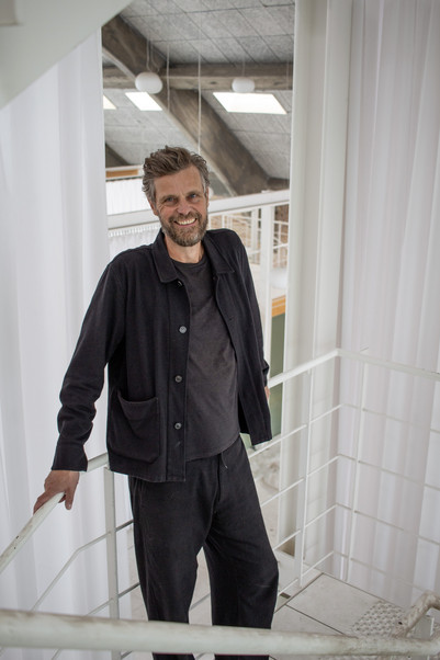 Person iført mørkt tøj står på en hvid trappe i et lyst interiør med store bjælkekonstruktioner