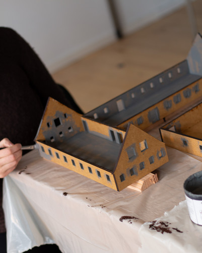 Hånd, der maler en arkitekturmodel af en bygning i pap eller træ.