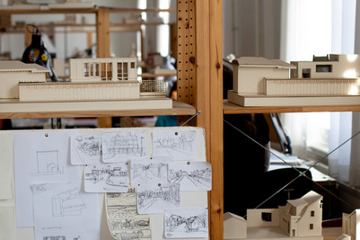 Arkitektmodel og skitser på opslagstavle i studie- eller værkstedsmiljø.