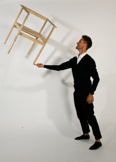 Person balancerer en træstol på en finger i et fotostudie.