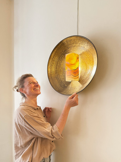 erson undersøger vægmonteret lampe med gylden skærm.