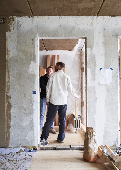To personer arbejder i et rum under ombygning med byggematerialer.