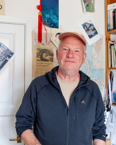 Person står i et rum med kort, fotos og opslag på væggen bag sig