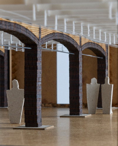 Architectural model with brick arches, timber elements, wires, and human figures.