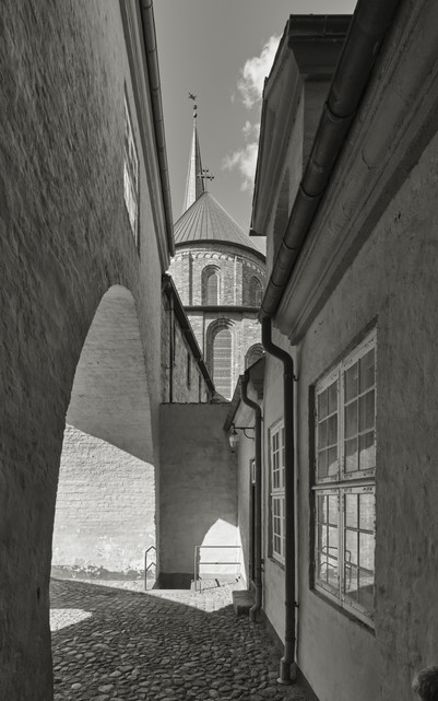 Narrow cobbled passage between old buildings, with a view of a church dome and spire.