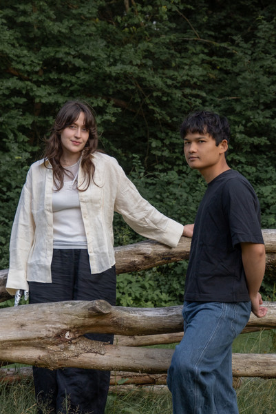 Two people standing by a wooden fence with dense woodland behind them.