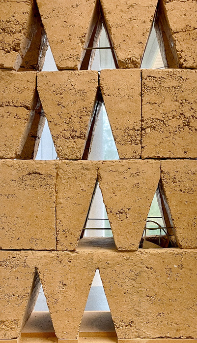 Sandfarvet facade med geometriske, trekantede åbninger.