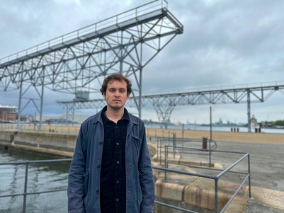 Man standing in front of large industrial steel structures by a harbor.