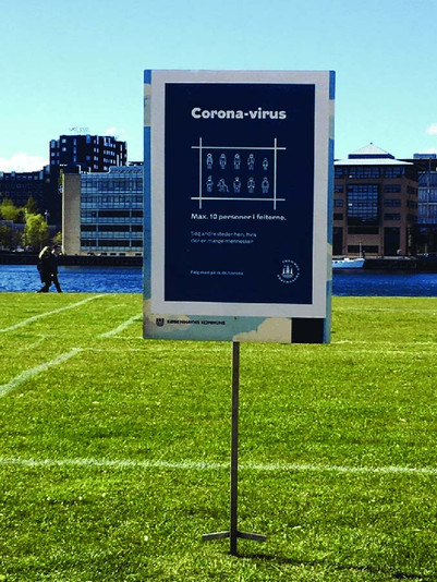 Skilt på græsplæne med corona-afstande markeret