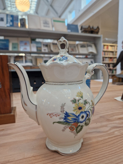 Hvid porcelænskande med låg, buet hank og farverige blomstermotiver.