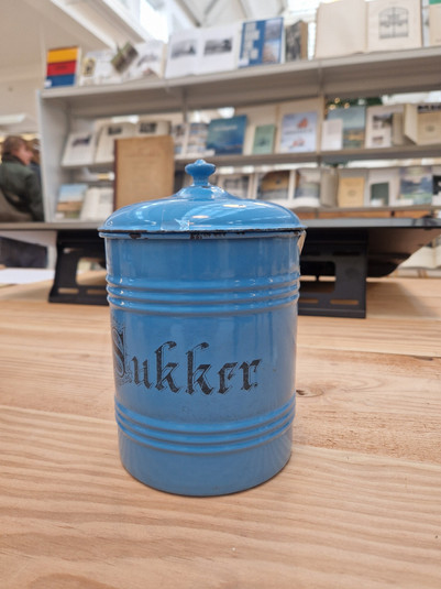 Blå cylindrisk metalbeholder med låg og påskriften »Sukker«.